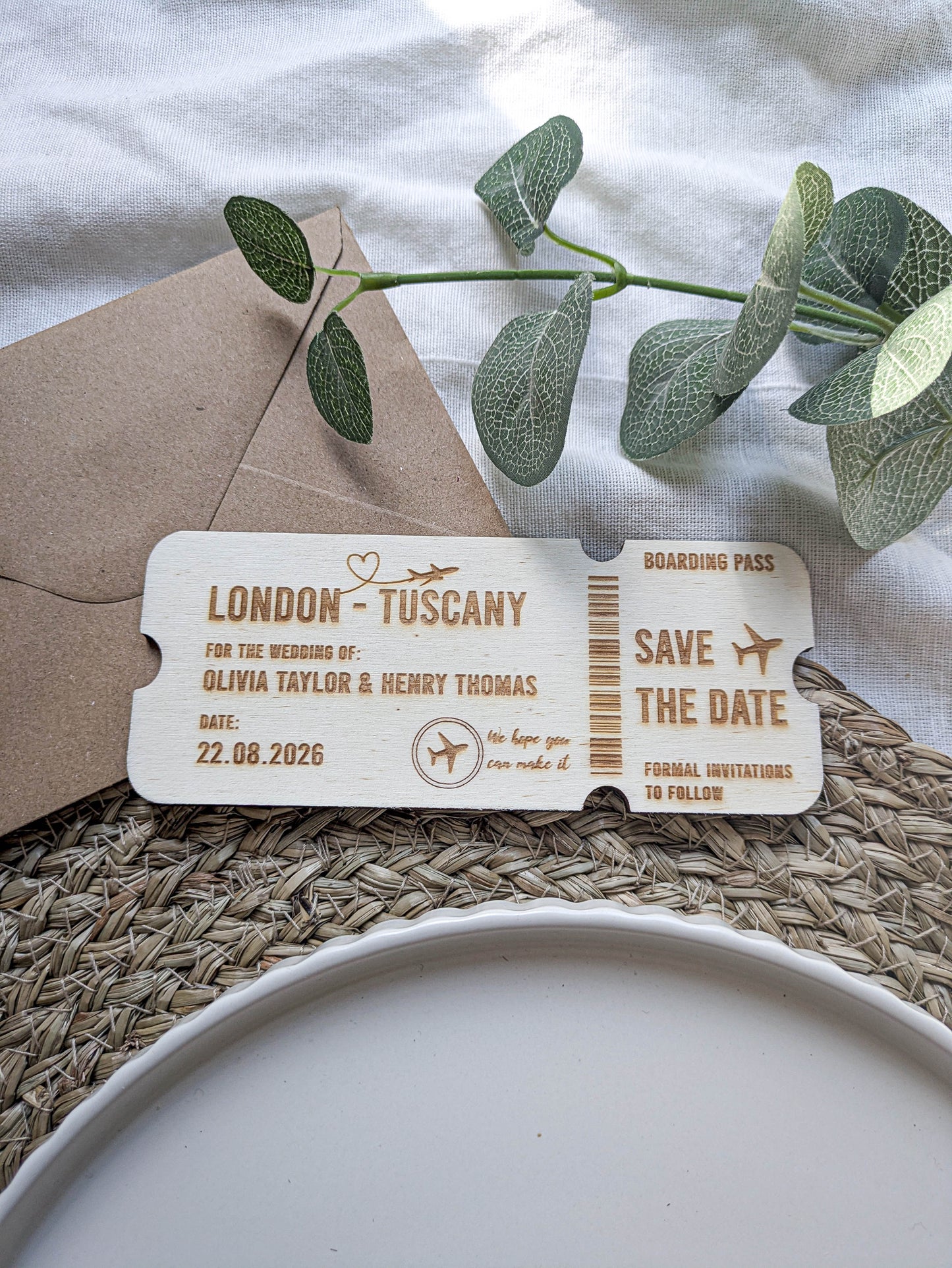 Engraved wooden save the date boarding pass shown with a kraft envelope